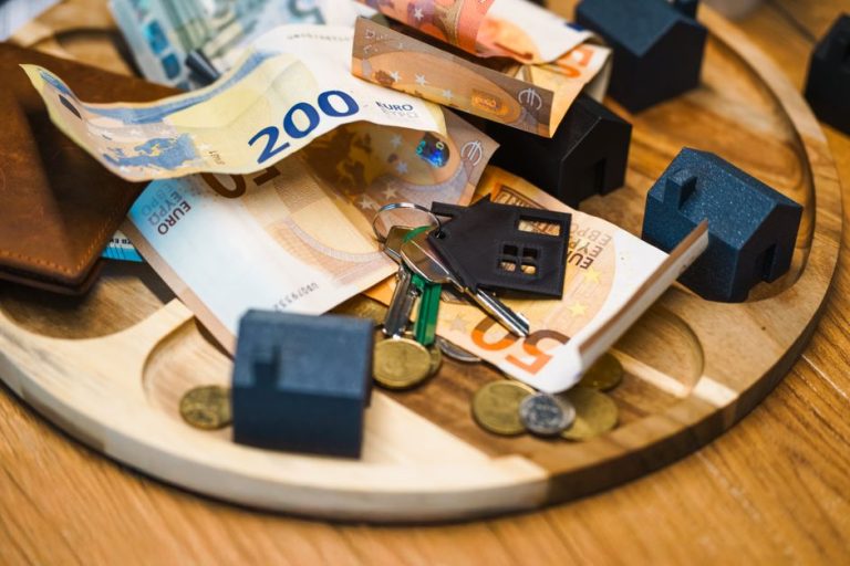 Мініатюрні будиночки, ключі та монети на столі як символ інвестицій у нерухомість